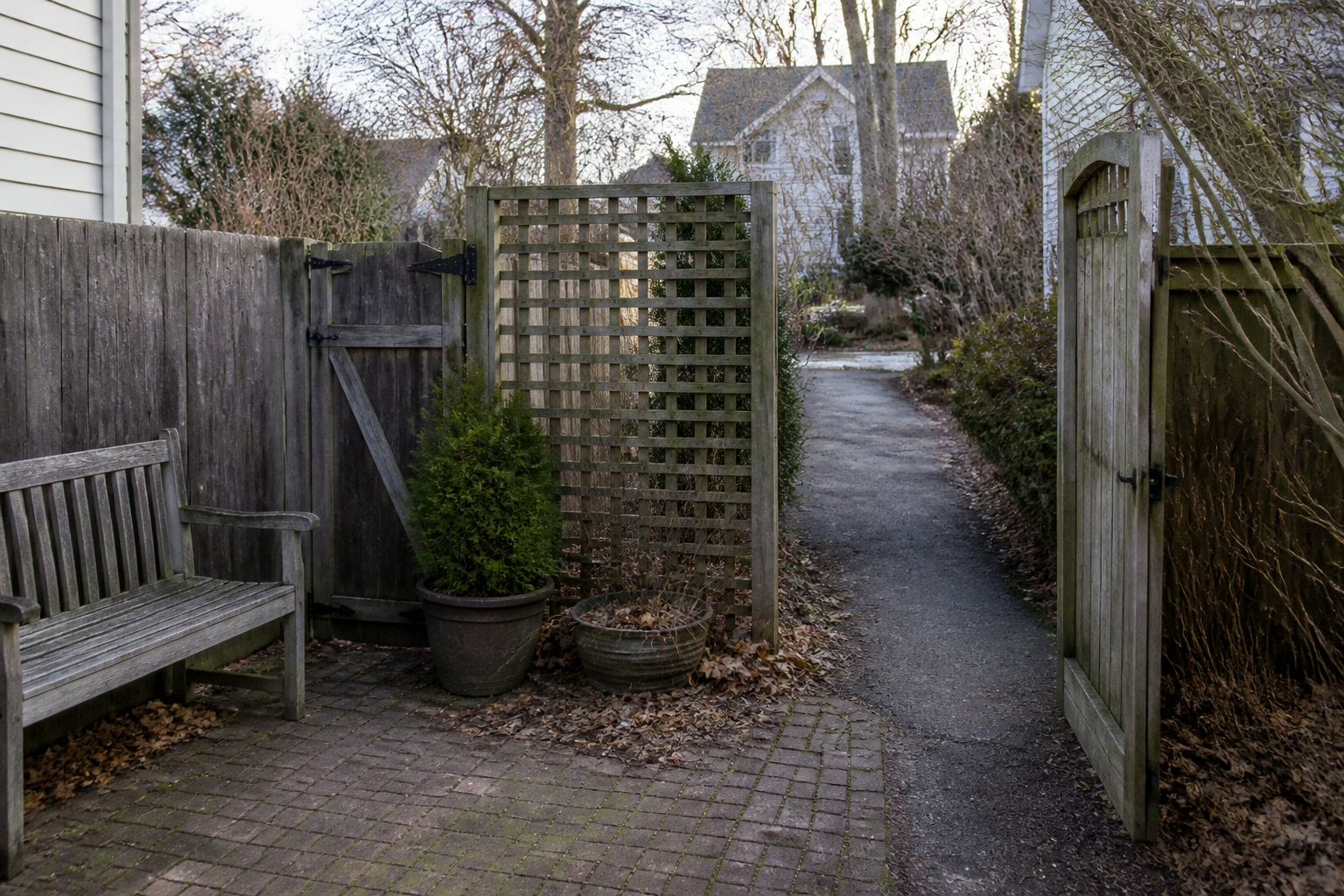Small winter patio with a lattice screen beside a bench and an open gate and path