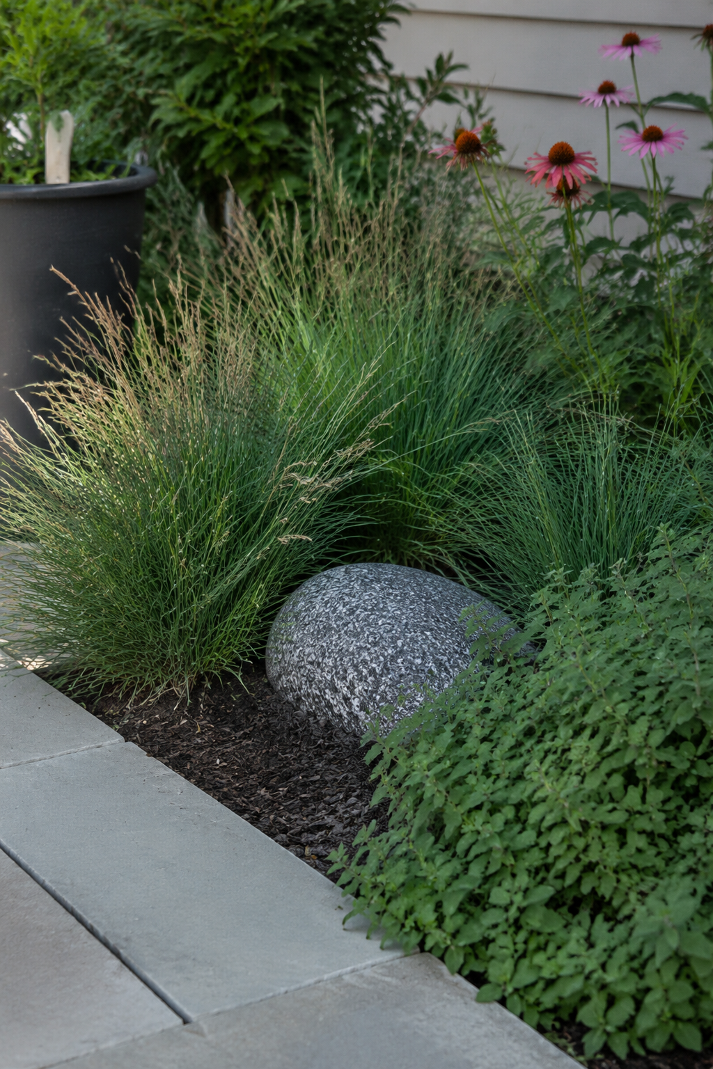 In-ground landscape speaker styled to look like a rock, partially hidden in a flower bed at the corner of a patio