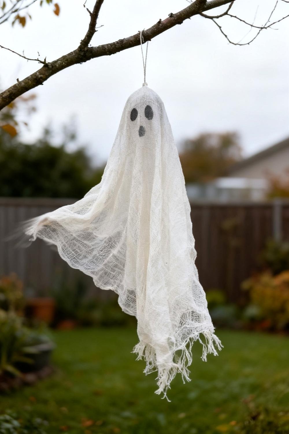 A small white gauze ghost drying over a balloon taped to a dowel on a kitchen table, folds hanging in soft daylight from a window