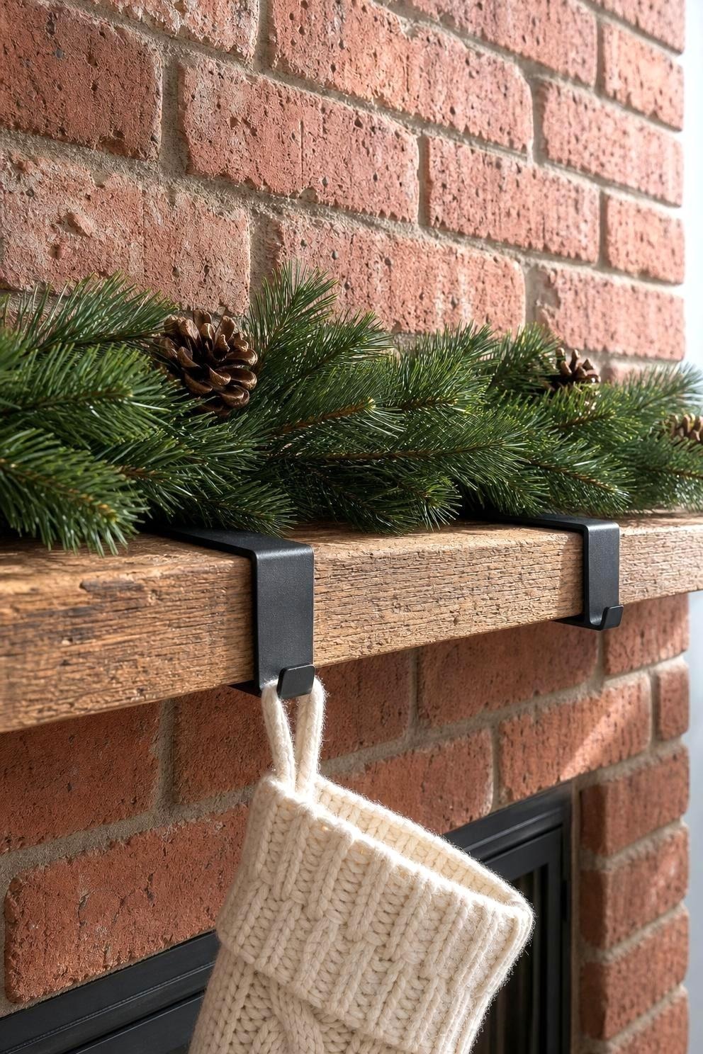Evergreen garland held to a red brick fireplace mantel by black metal mantel clips gripping the shelf edge