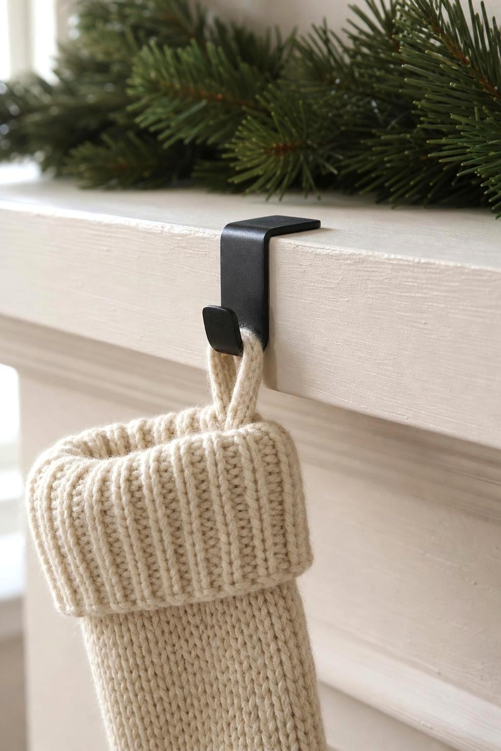 Close view of a metal stocking holder gripping the edge of a painted wood mantel with a knitted stocking hanging from it