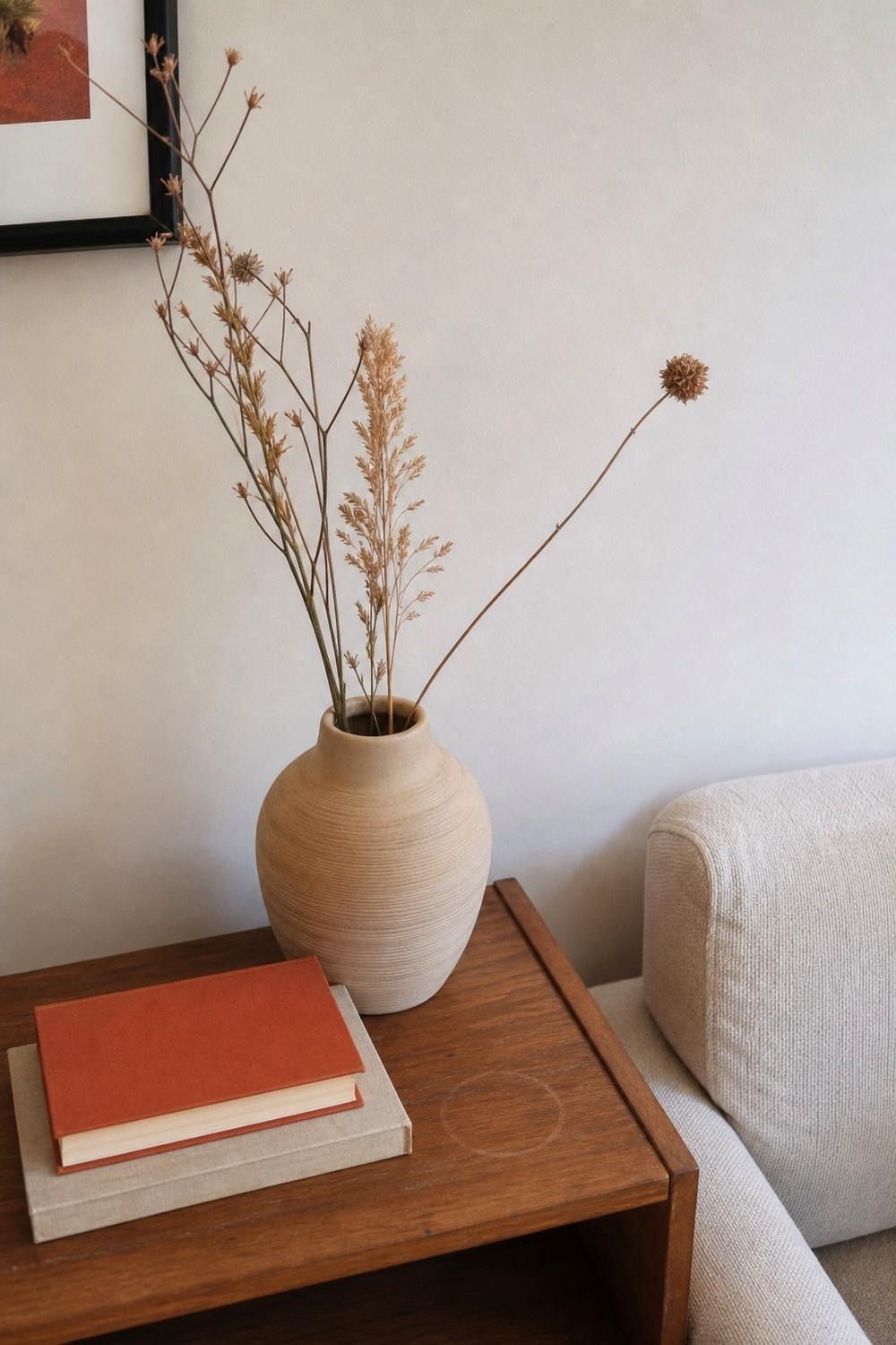 Beige ceramic vase with dried stems on a living room shelf