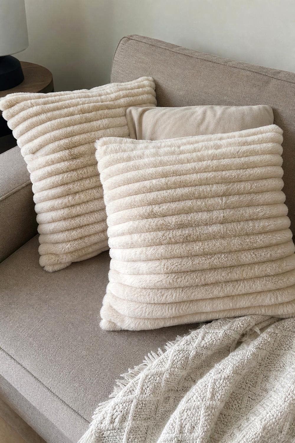 Cream faux fur throw pillow covers layered on a sofa with a rust pillow
