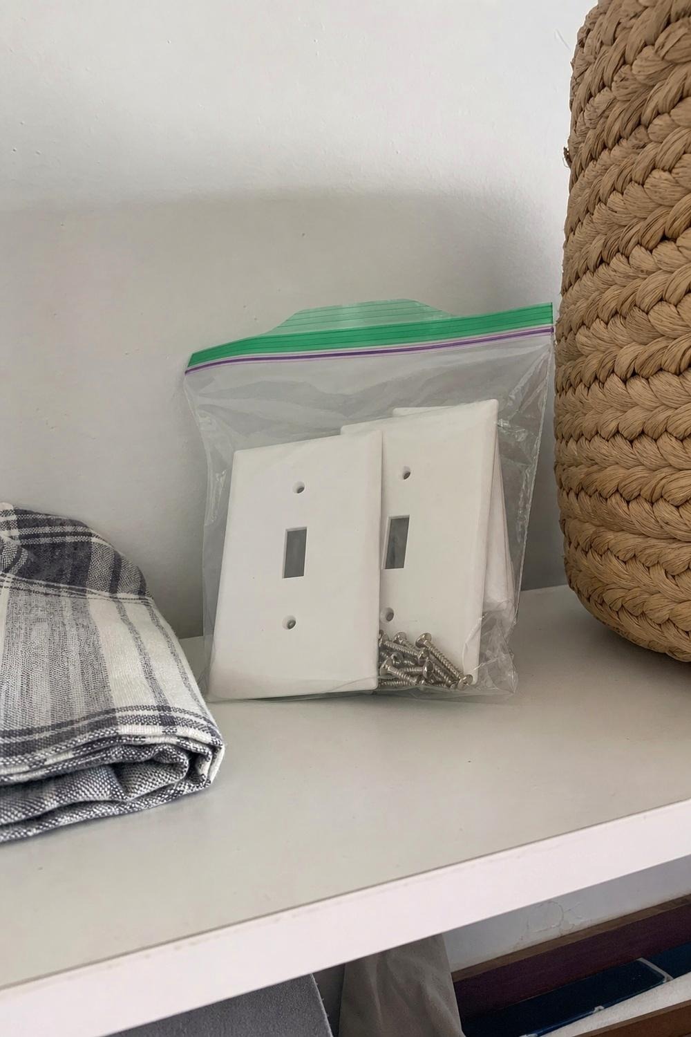 labeled zip bag holding an original white switch plate and screws next to a new brass plate