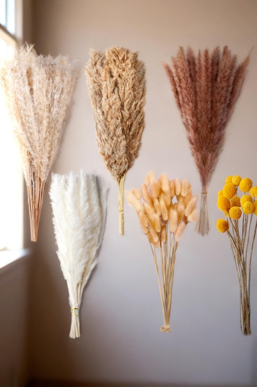 Close detail of dried wreath texture, pale wheat heads, a grass plume and small papery statice bracts against a woven grapevine base, soft daylight