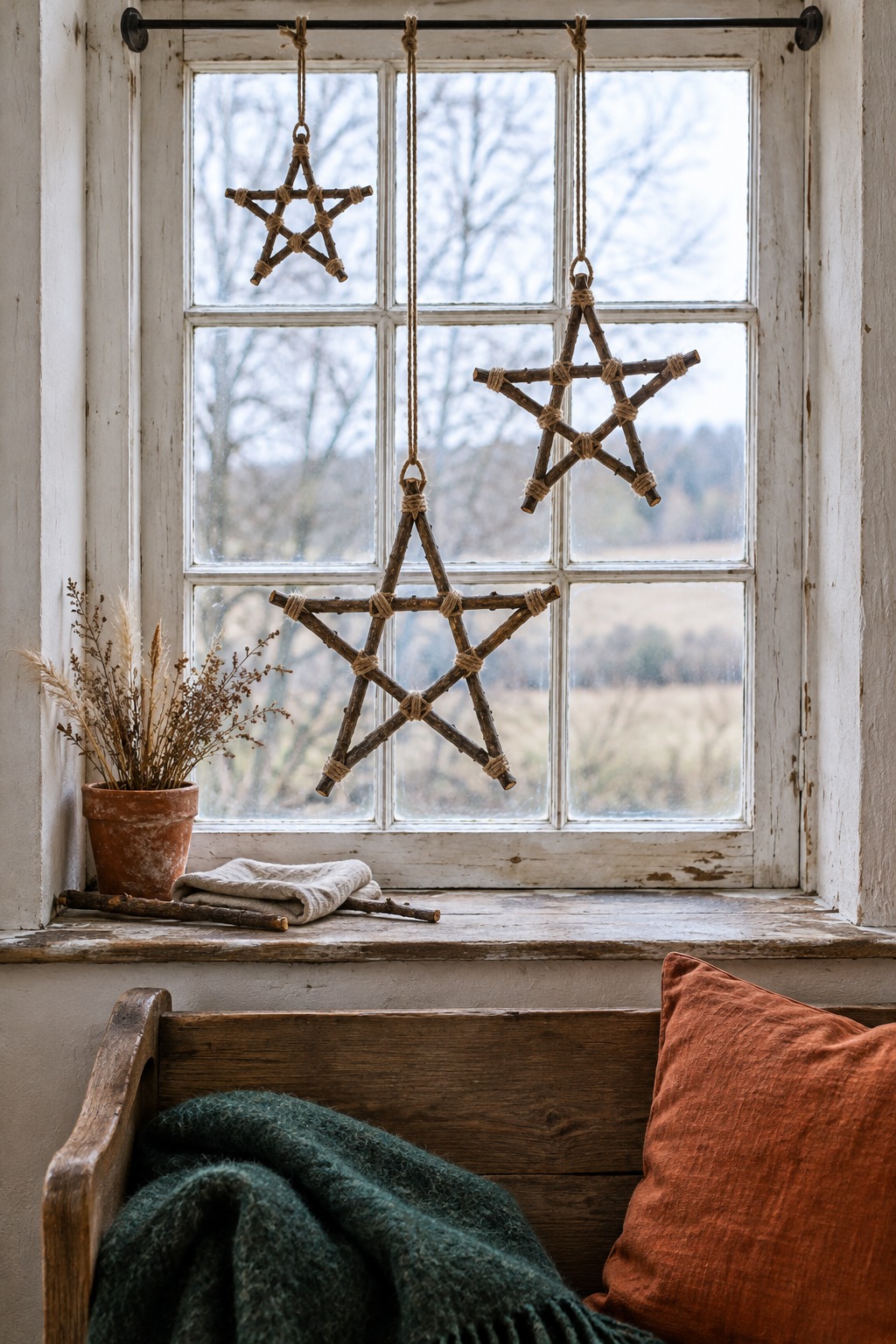 Three rustic stars made of five bare twigs each, glued and wrapped with jute twine, hanging at different heights from twine in a window