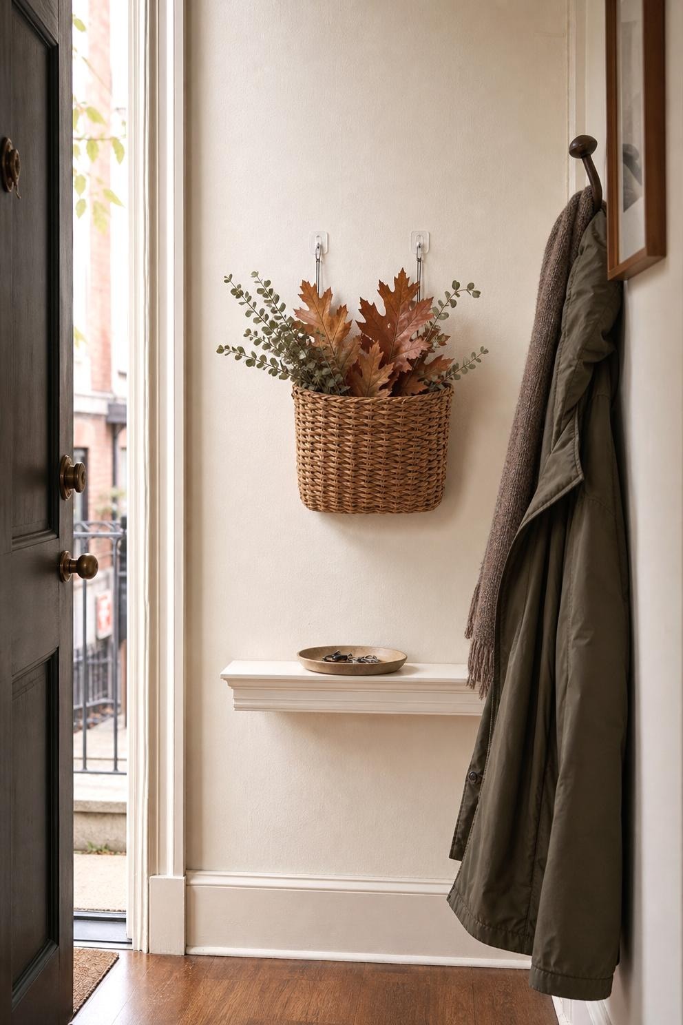 Removable wall hooks holding a light woven basket with rust leaves above a narrow entry ledge