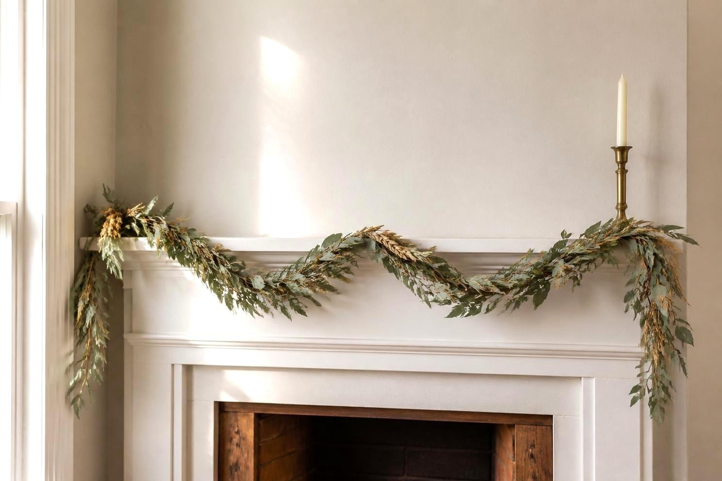 A neutral eucalyptus and dried wheat garland draped along a white painted mantel shelf with two shallow dips and longer tails hanging at each end, lit by afternoon window light