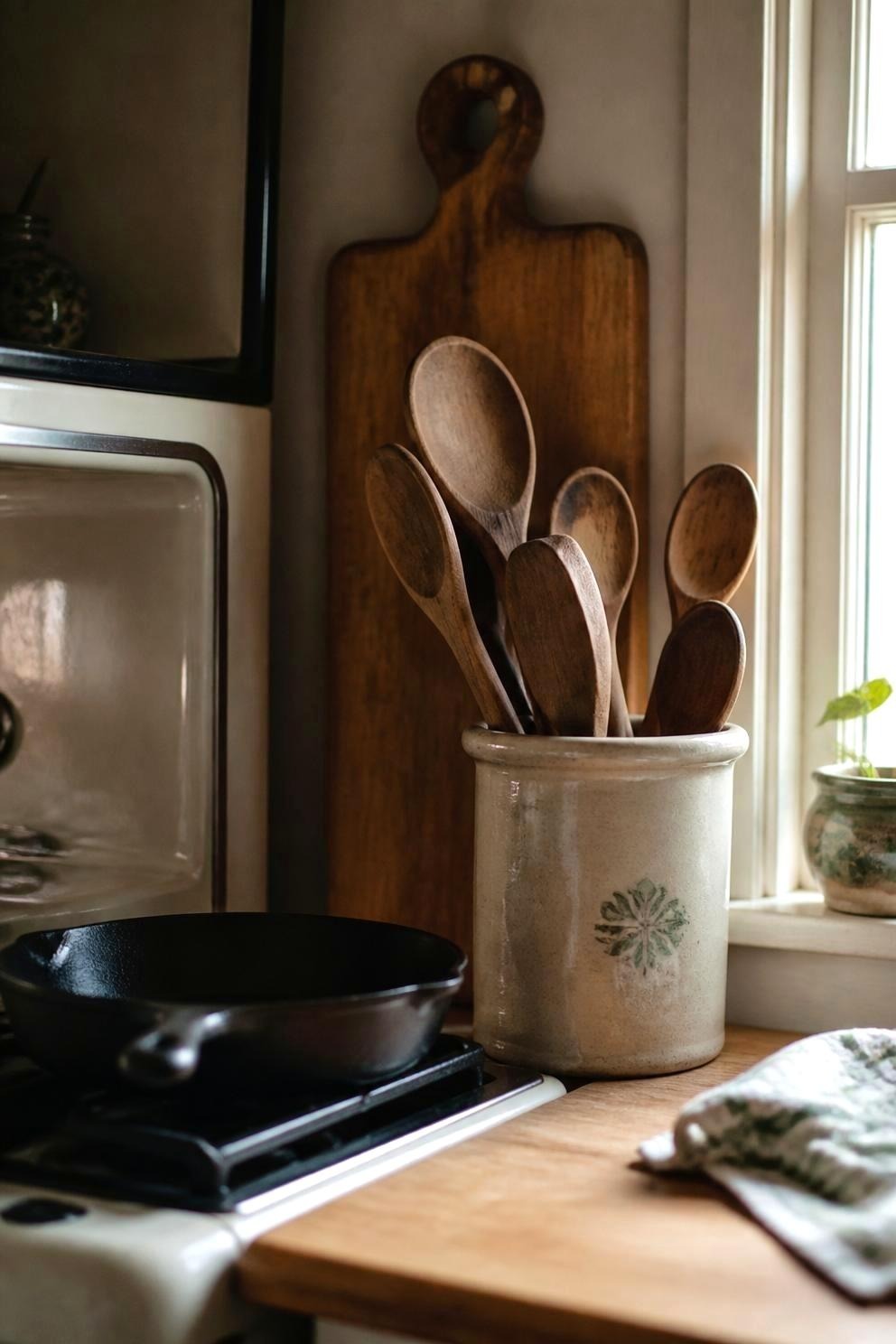 wooden spoons in a stoneware crock beside a stove with a pot on the burner