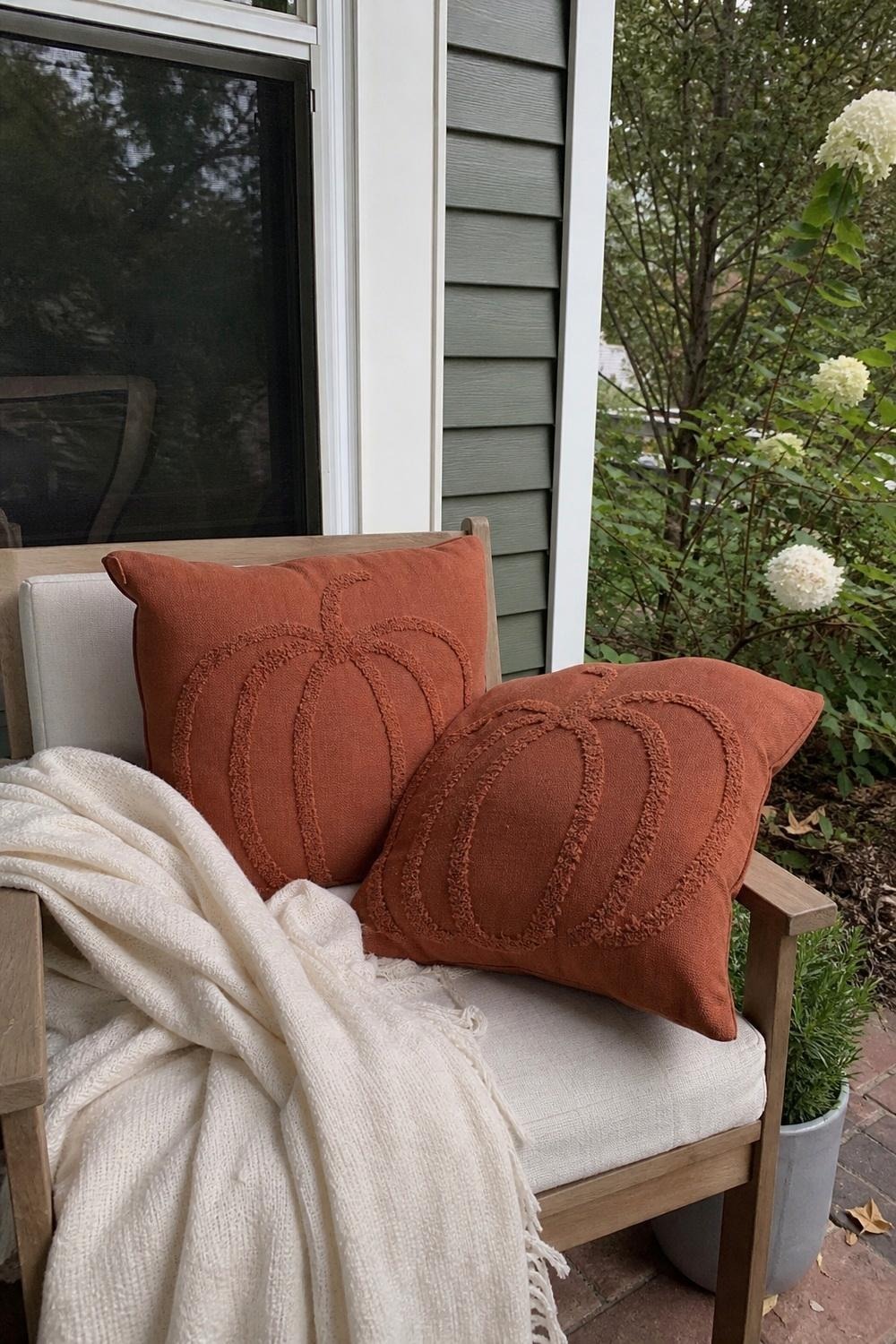Rust orange pumpkin-embroidered throw pillow on a porch chair, plush indoor-style fabric
