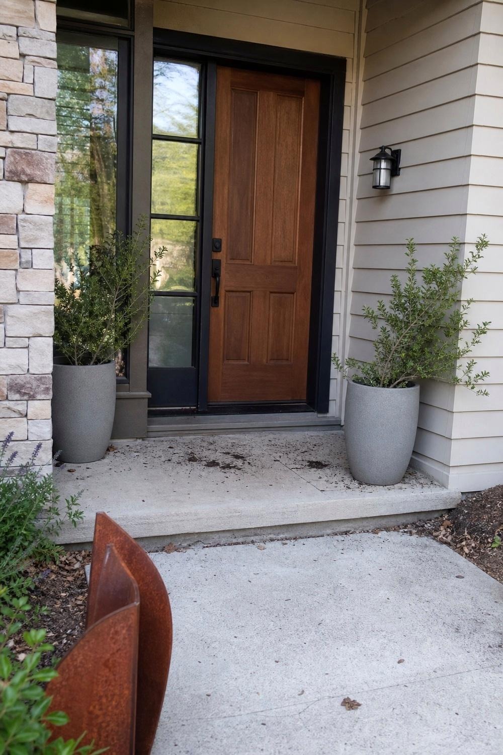 Two tall stone-look round planters flanking a front porch entry, one holding a small shrub