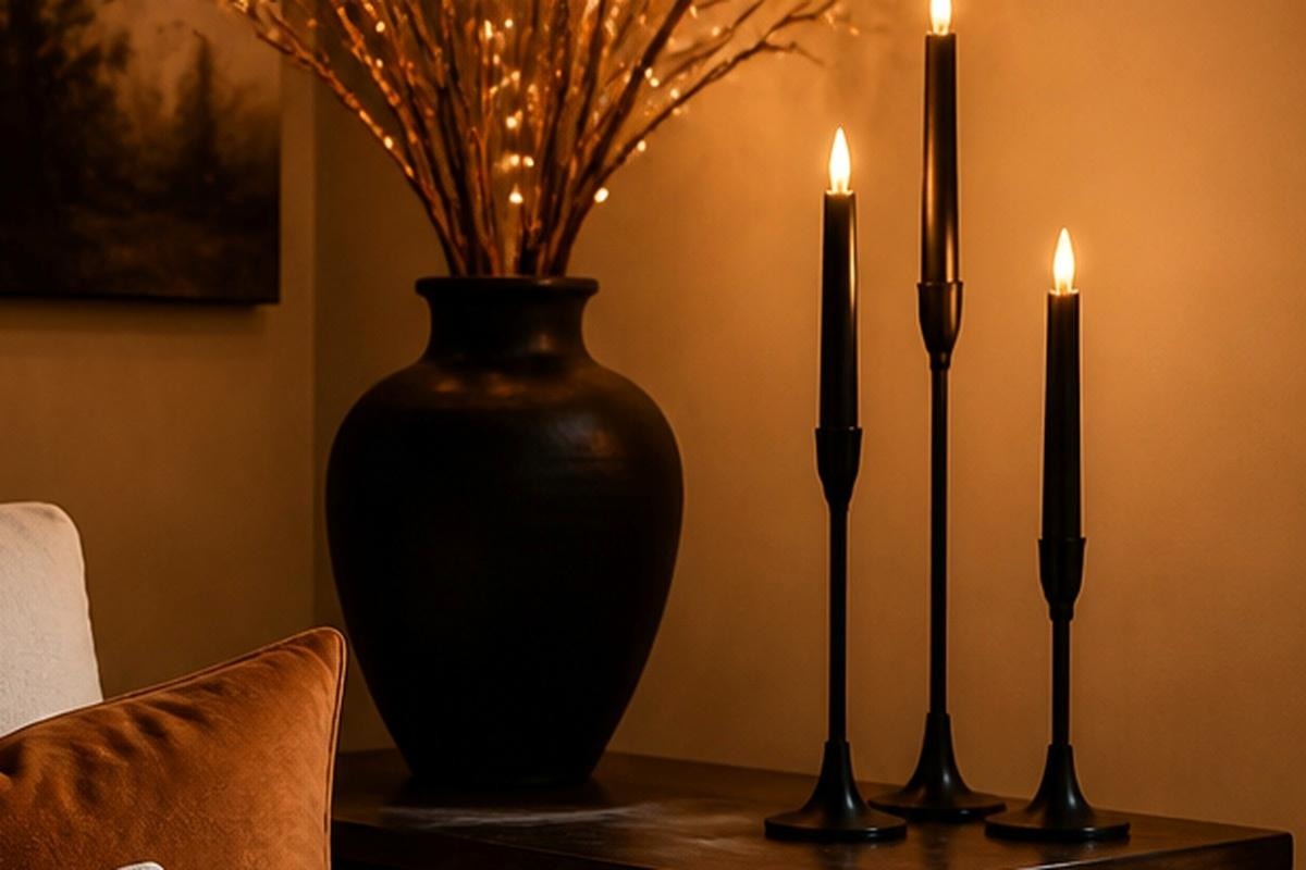 Three matte black candlestick holders in staggered heights on a cream fireplace mantel