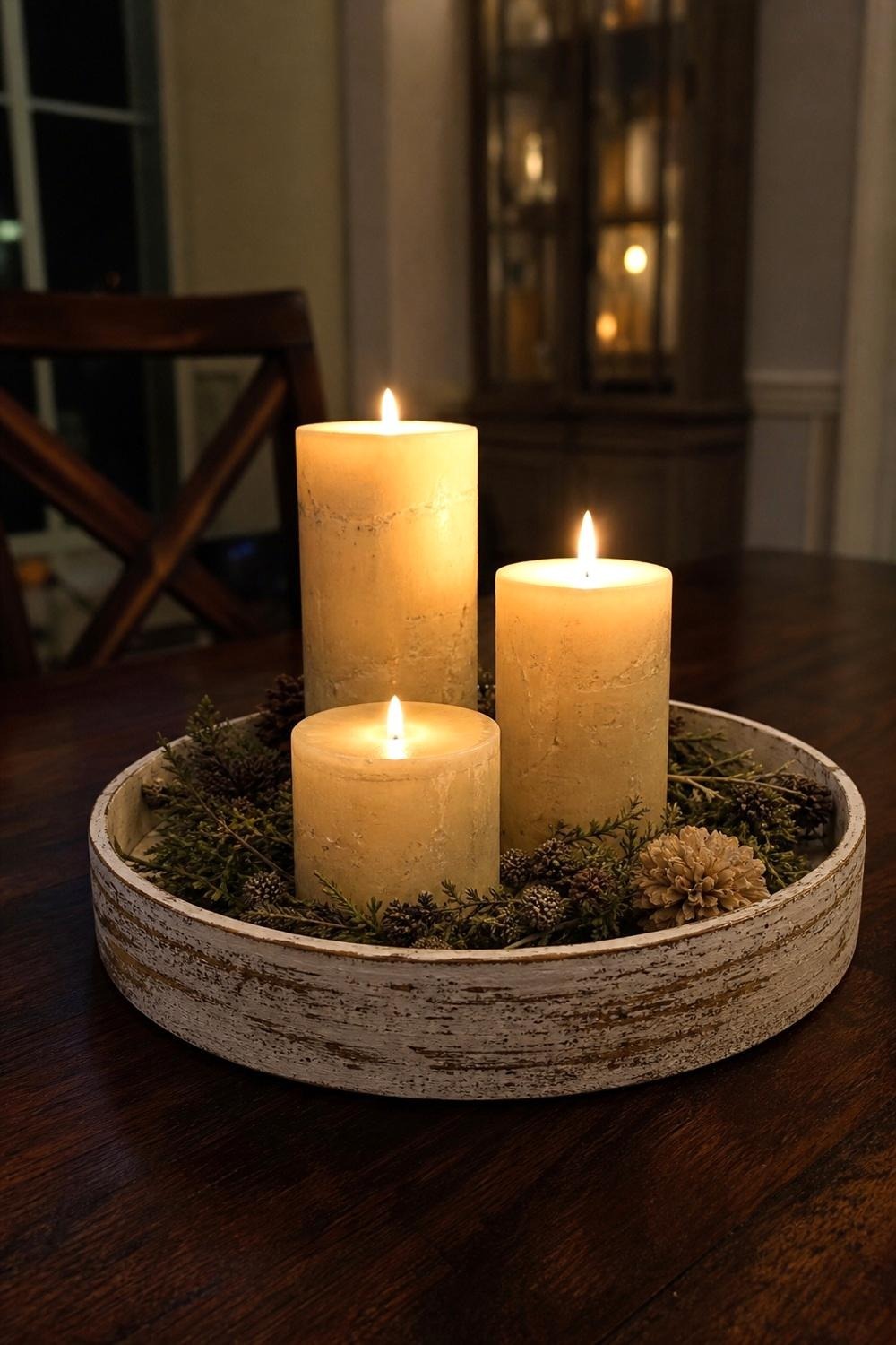 Round distressed wood tray holding candles and small decor at the center of a dark dining table
