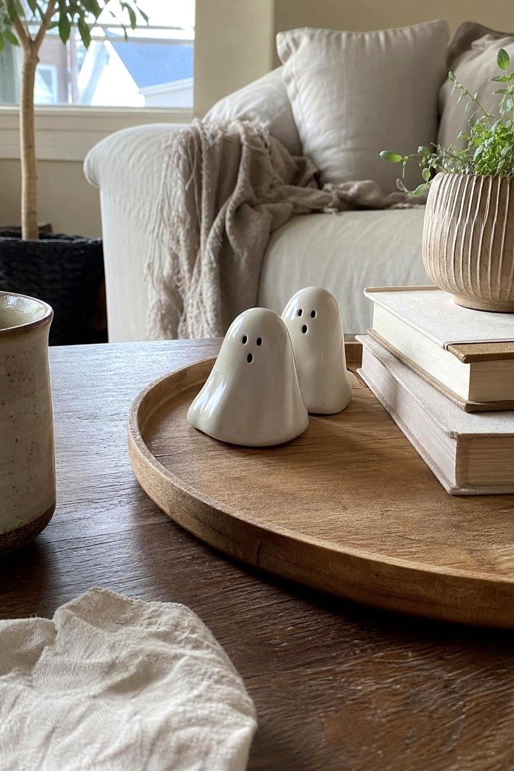 Two small white ceramic ghost figurines on a wooden tray