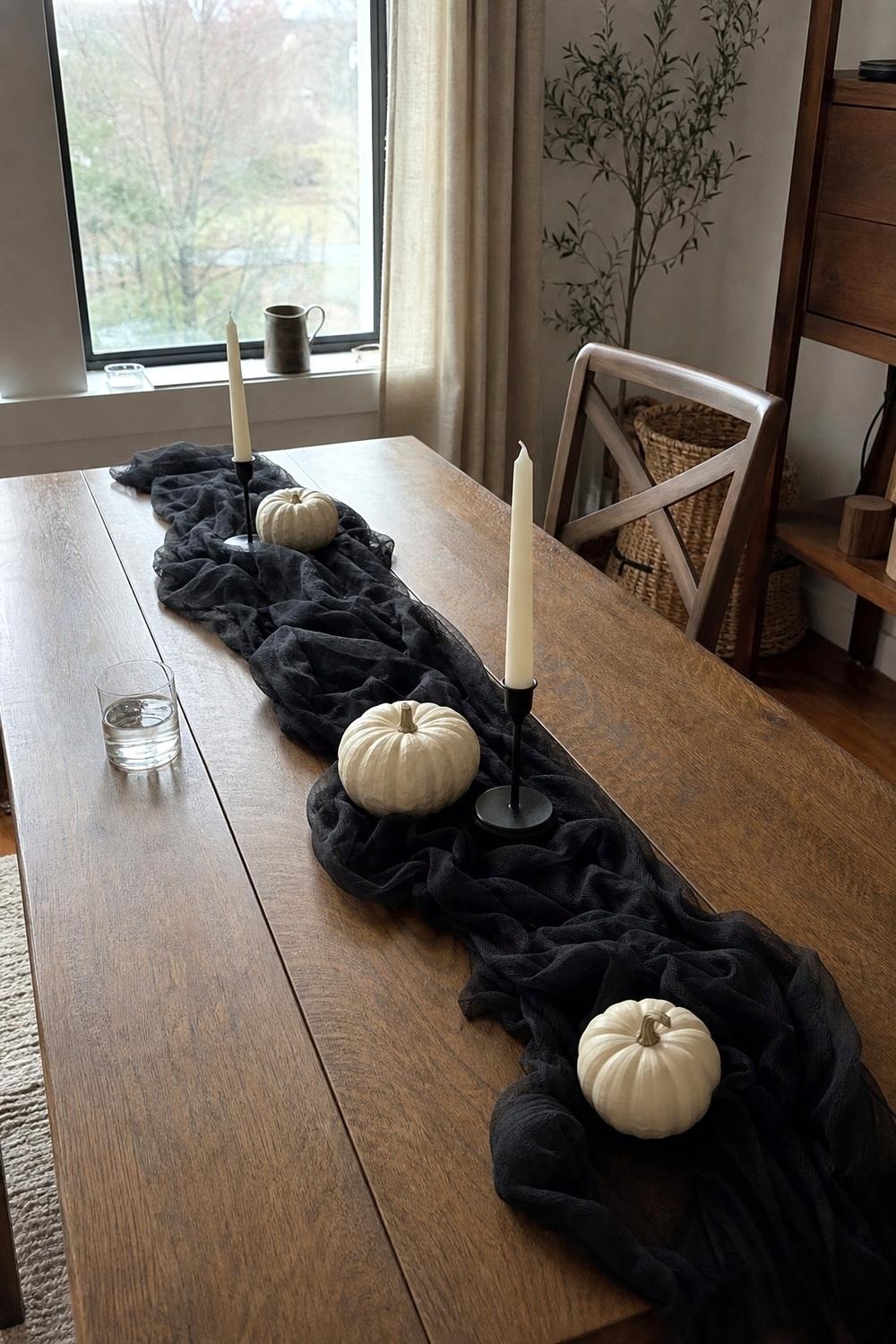 Black cheesecloth runner bunched down a wooden dining table with white pumpkins and candles