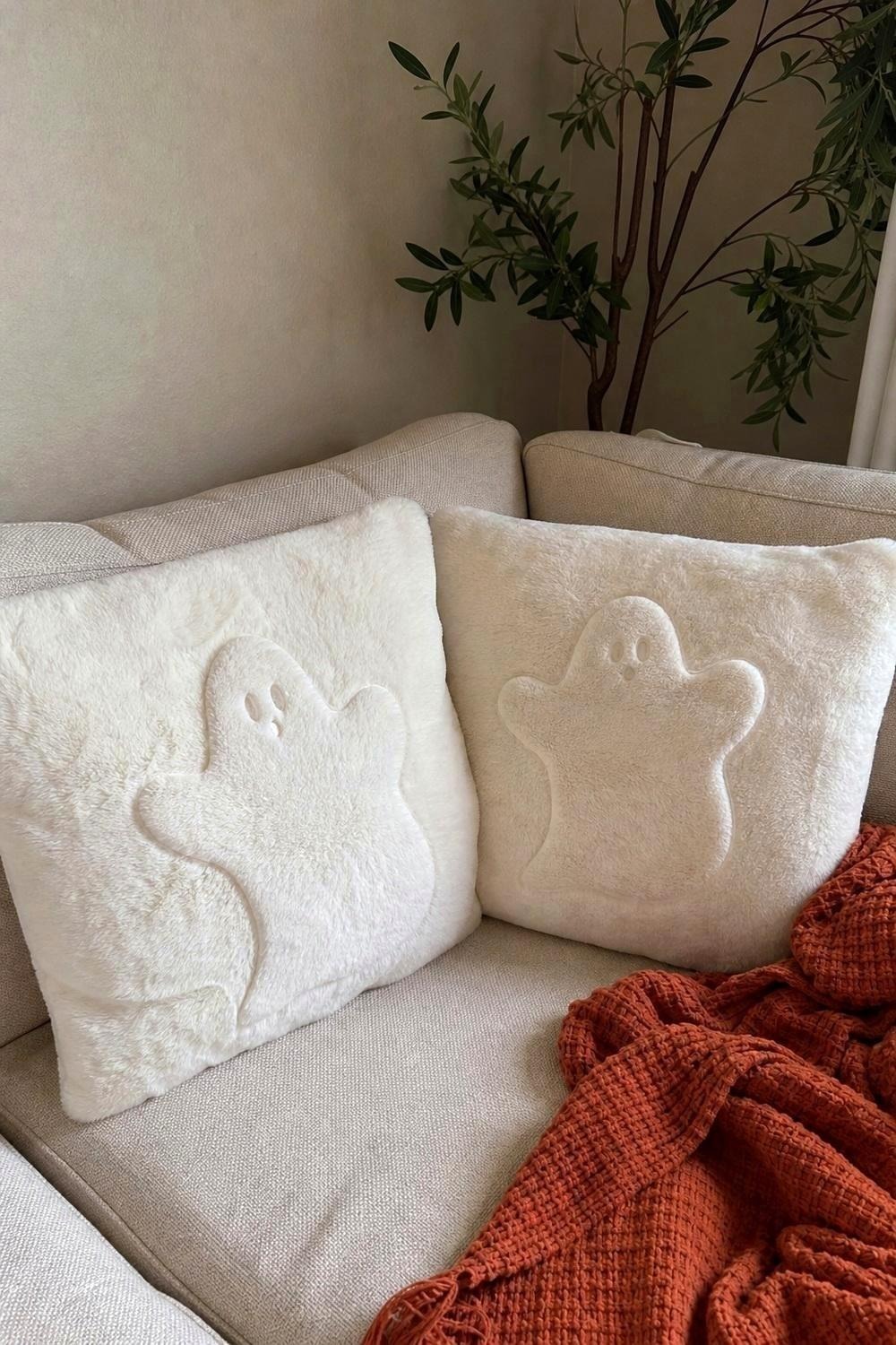 Two white ghost faux fur pillow covers on a cream sofa
