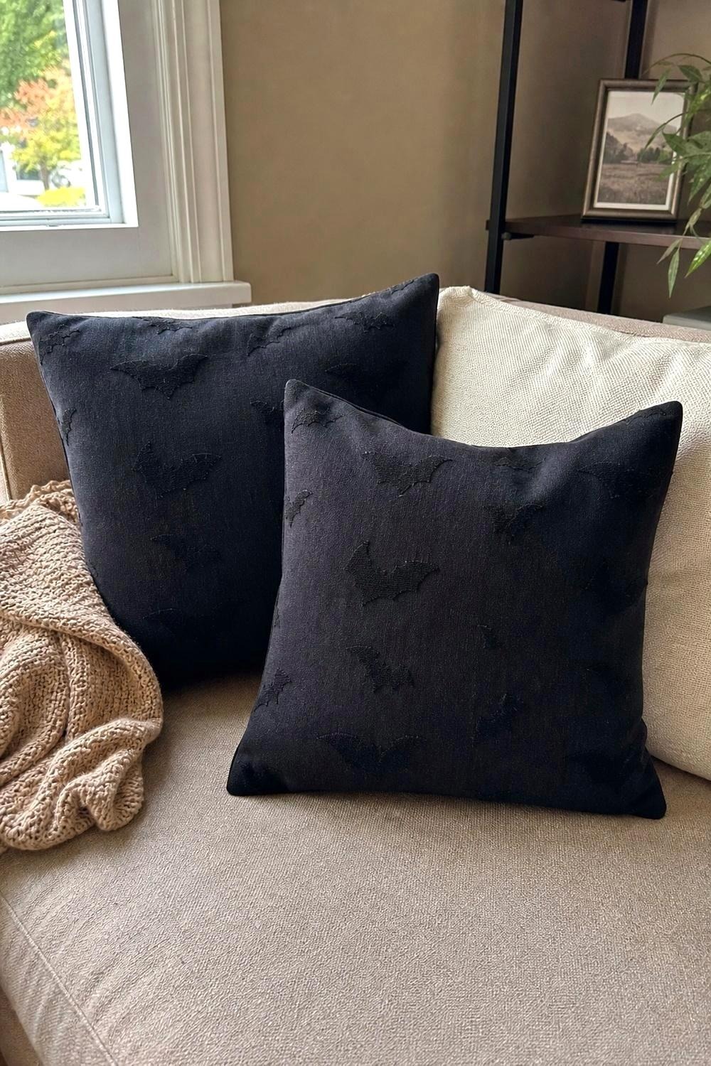 Black bat jacquard pillow covers layered on a neutral sofa