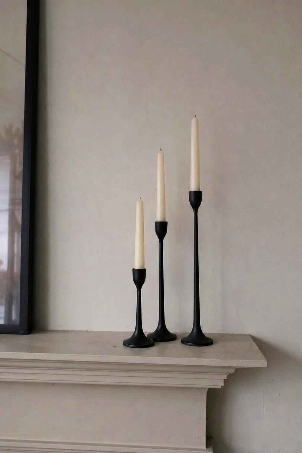 Three matte black metal taper candle holders at different heights on a mantel