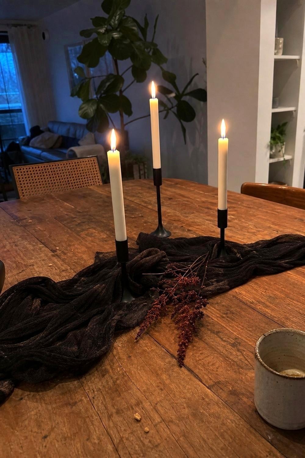 Ivory flameless taper candles lit in black holders beside a draped runner