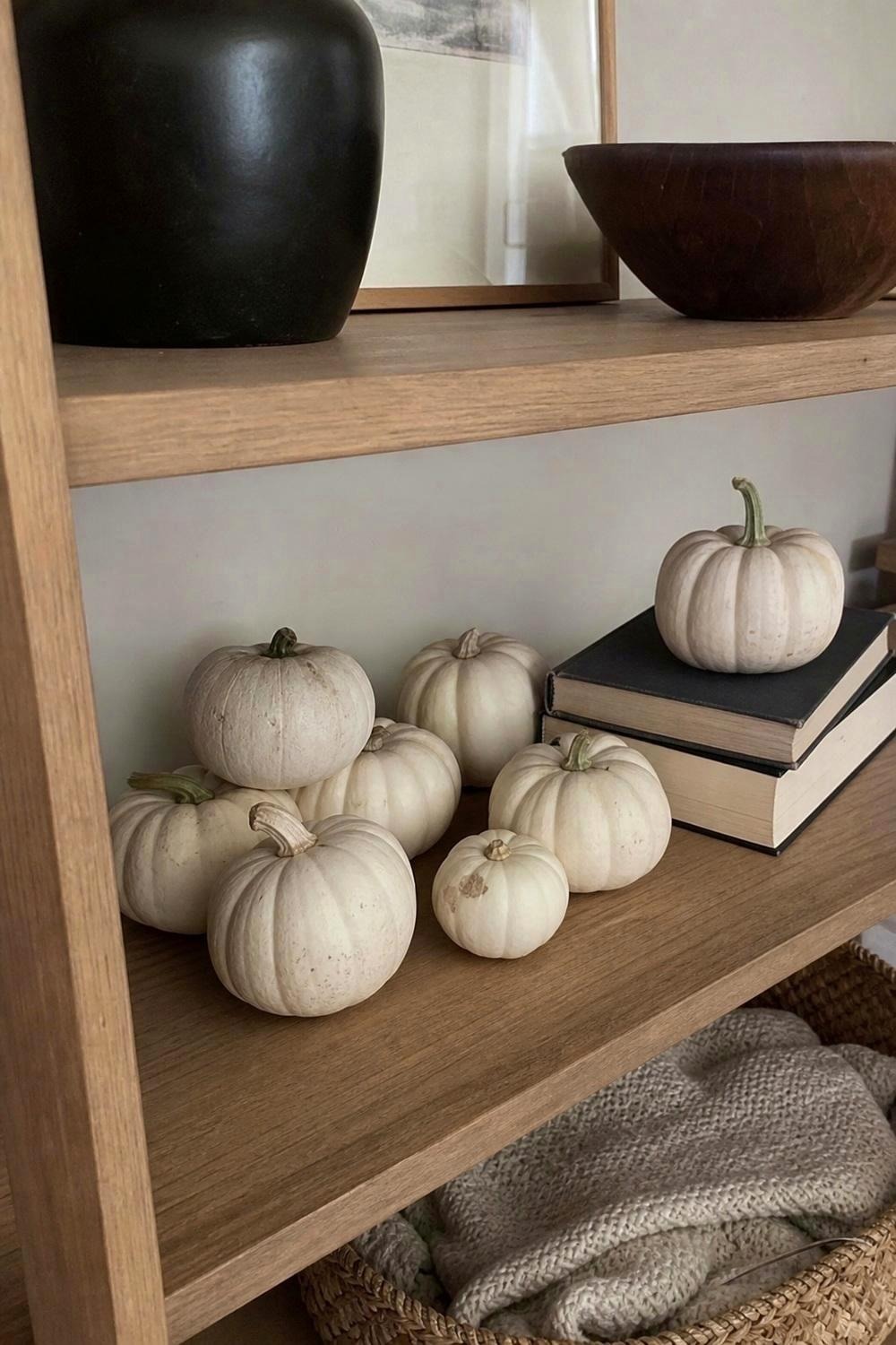 Small white artificial pumpkins in assorted sizes grouped on a wooden shelf