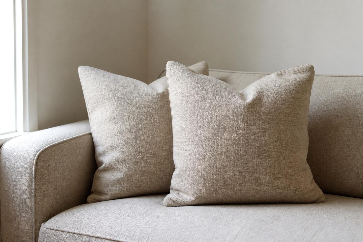 Two natural linen cushions propped in the corner of an oatmeal sofa