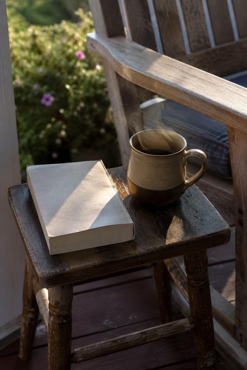 Small wooden stool beside a patio chair holding a coffee mug and book