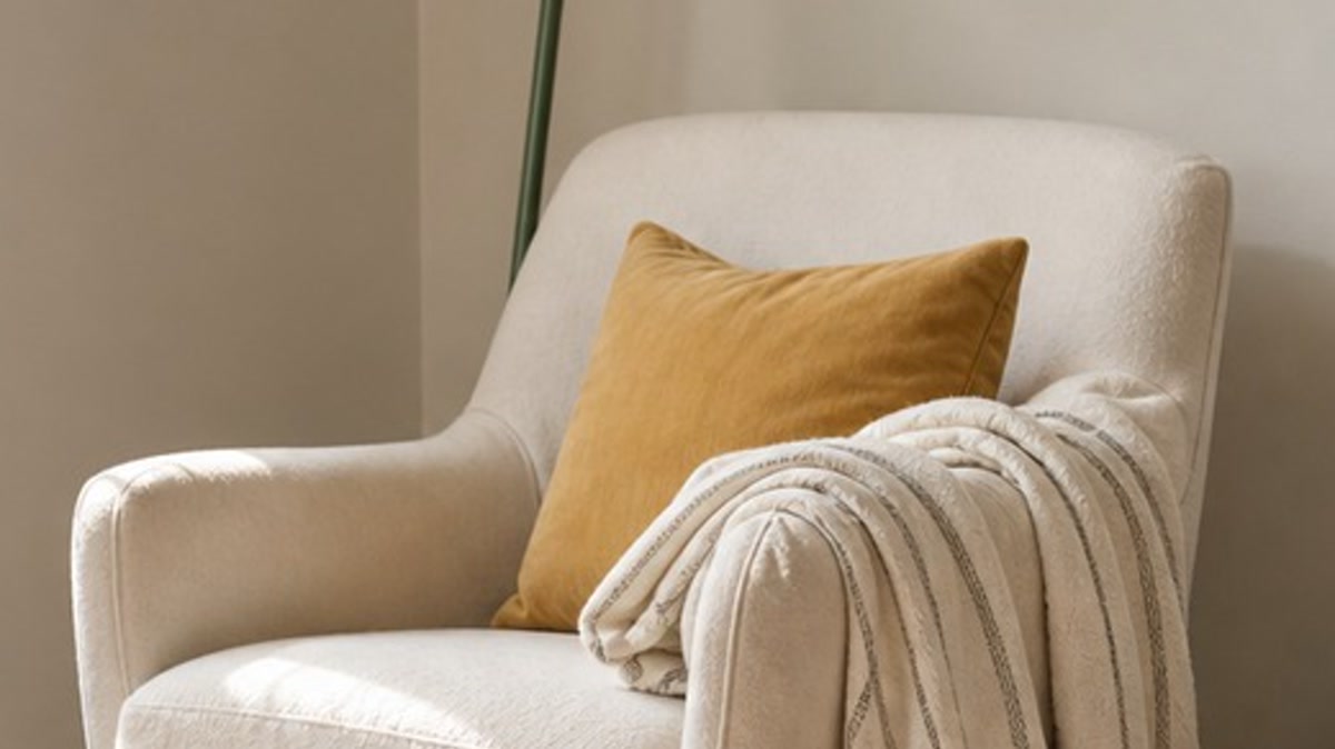 Muted ochre pillow centered on a cream reading chair beside an ivory throw