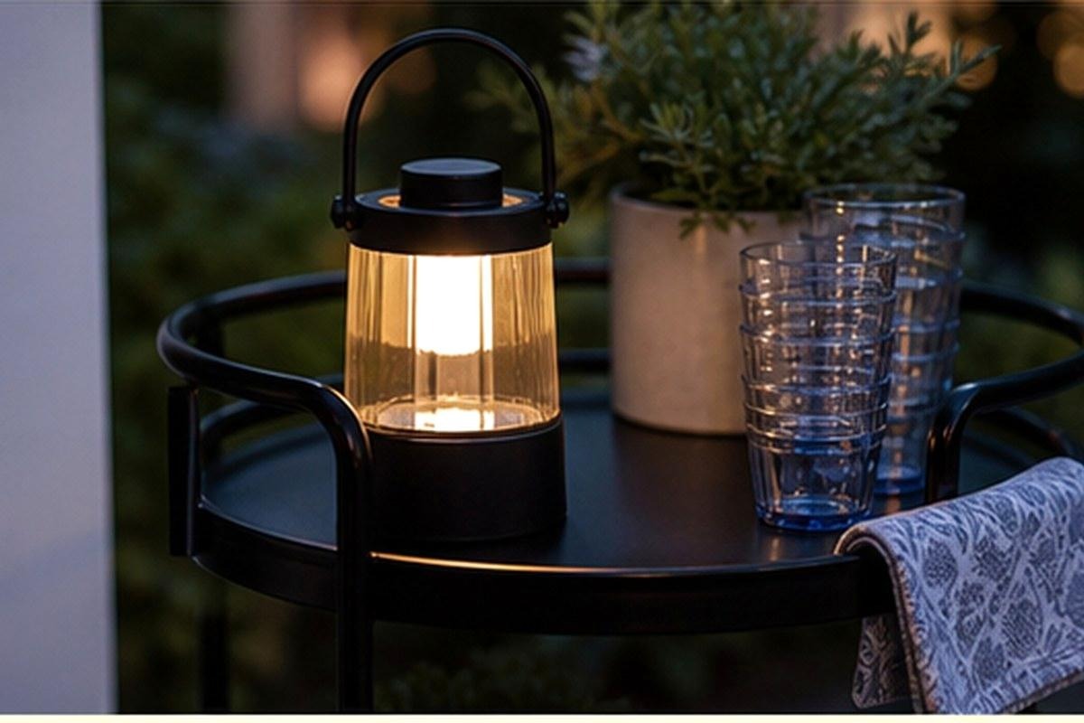 Compact black solar lantern glowing on a patio drink cart at dusk