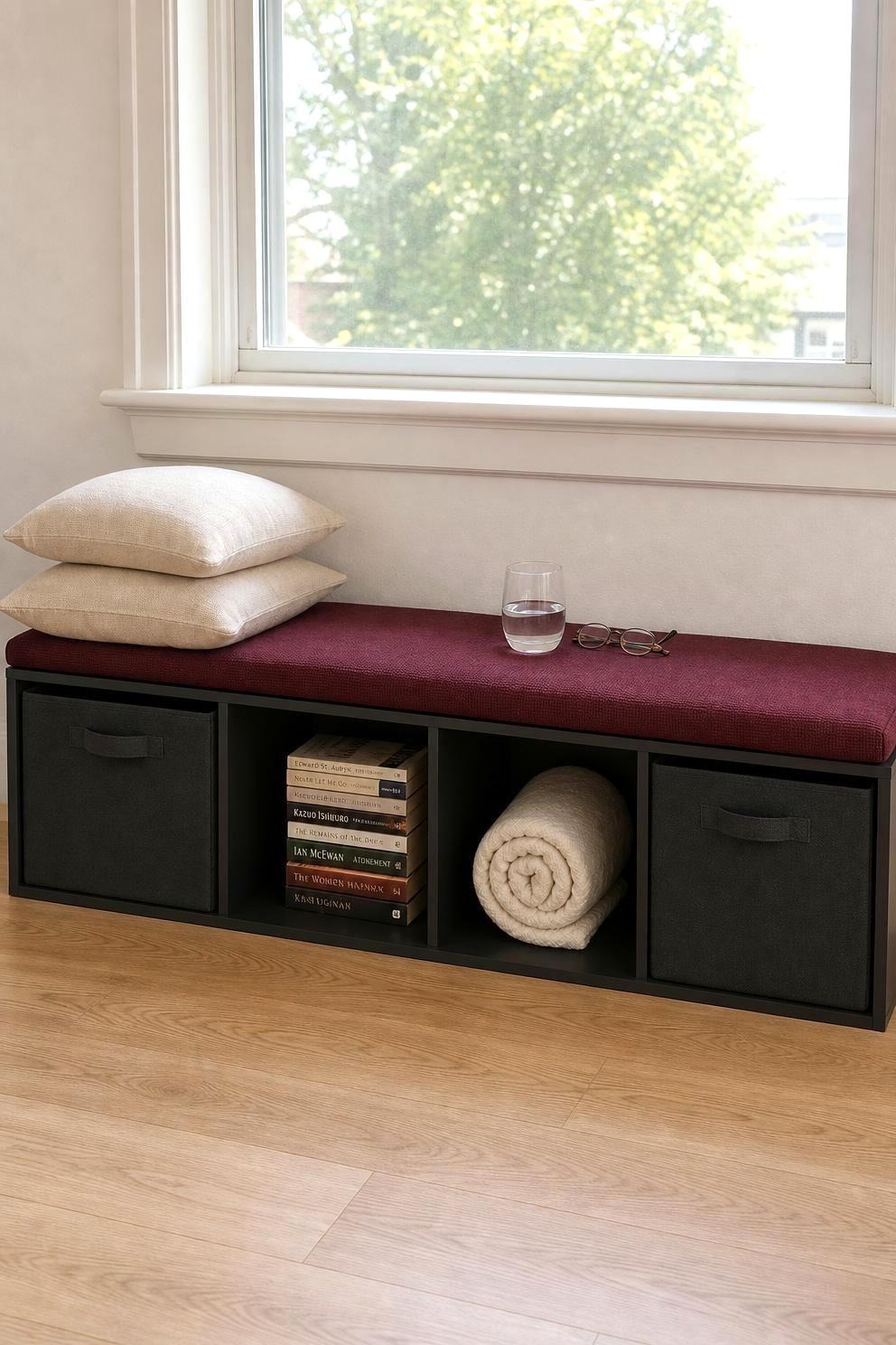 Four-cube shelf unit on its side under a window with canvas bins in the cubbies and a long burgundy cushion on top